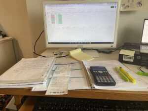 desk with a monitor, calculator, notebooks and receipt